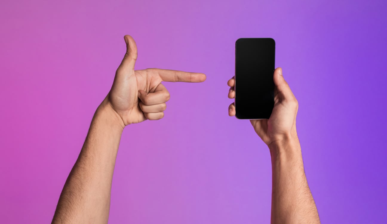 Closeup of young guy pointing at smartphone with empty black screen, showing space for new mobile app or website